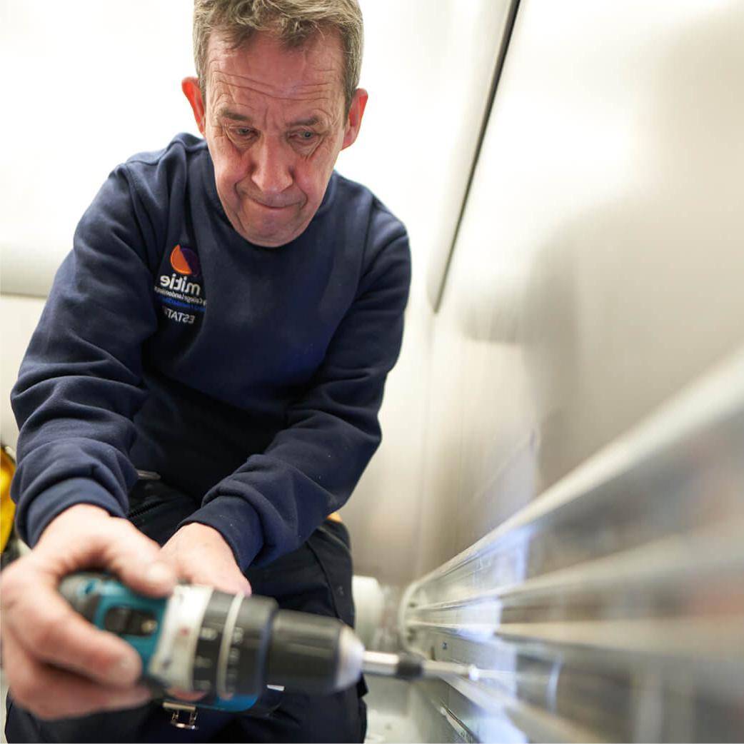 Mitie engineer using a drill and completing maintenance